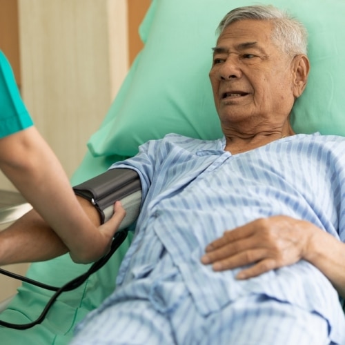 Senior,patient,lying,on,the,bed,and,nurse,measuring,blood